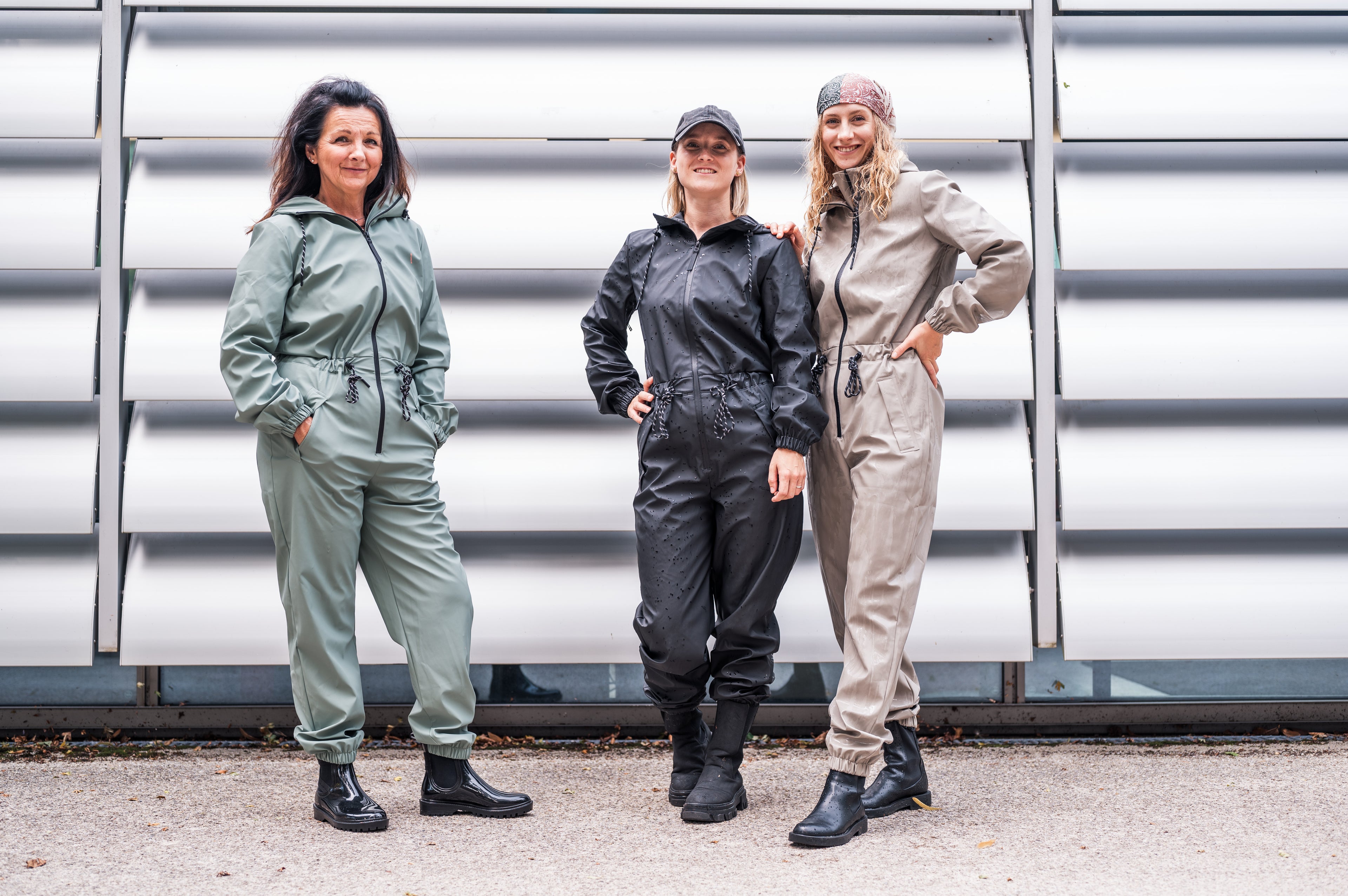 Three women wearing different types of jumpsuits standing against a metallic wall.